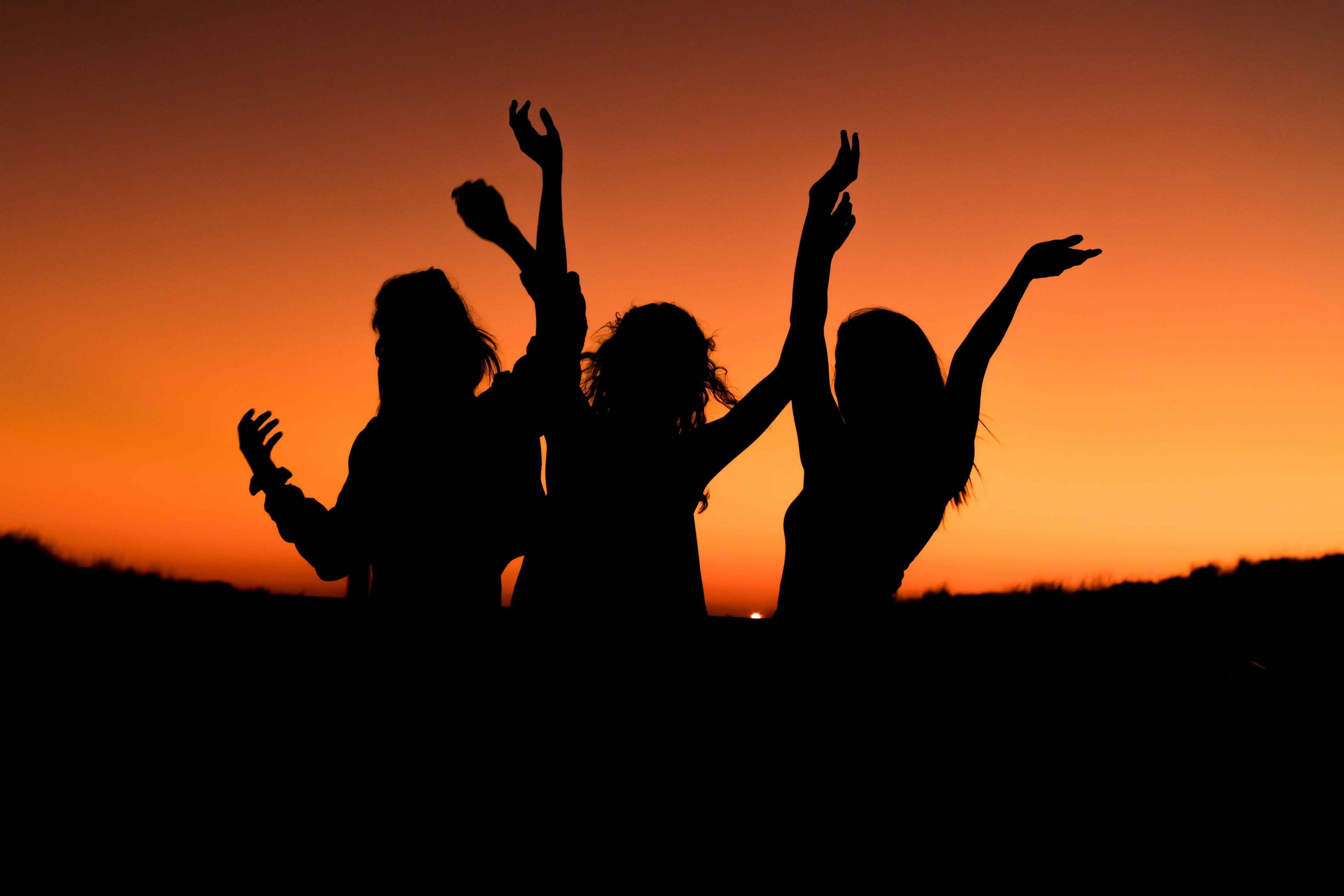 Silhouettes of three young people against an orange sunset